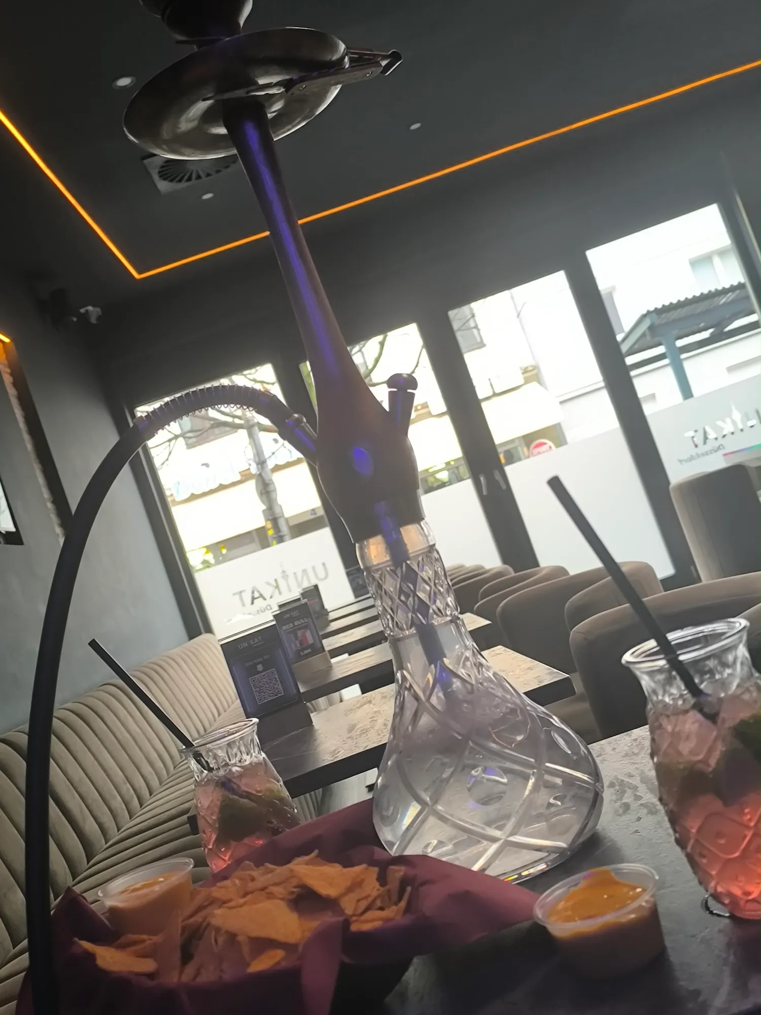 Shisha mit Kristallglas-Bowl auf dem Tisch, dahinter die Lounge mit Fensterfront