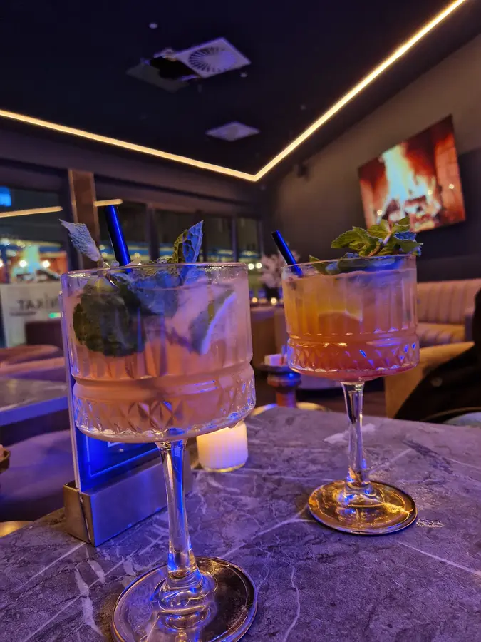 Zwei Cocktails mit Minze in Kristall-Stielgläsern auf einem Marmortisch im blauen Licht
