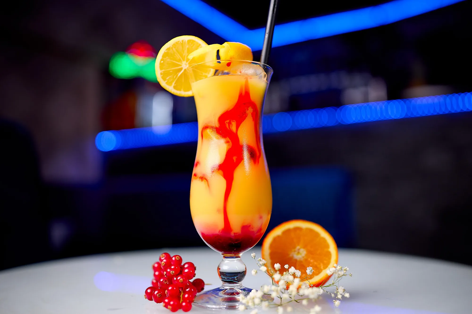 Fruchtiger Cocktail in Orange und Rot mit Orangenscheibe vor blauem Neonlicht