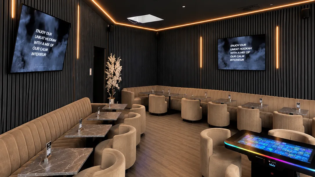 Lounge mit beigen Sesseln, dunklen Lamellenwänden und warmen Lichtleisten